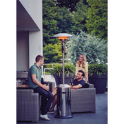 People sitting around a patio heater on a patio with greenery in the background