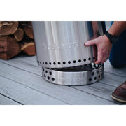 Silver Solo Stove on a wooden surface with a person's hand holding it.